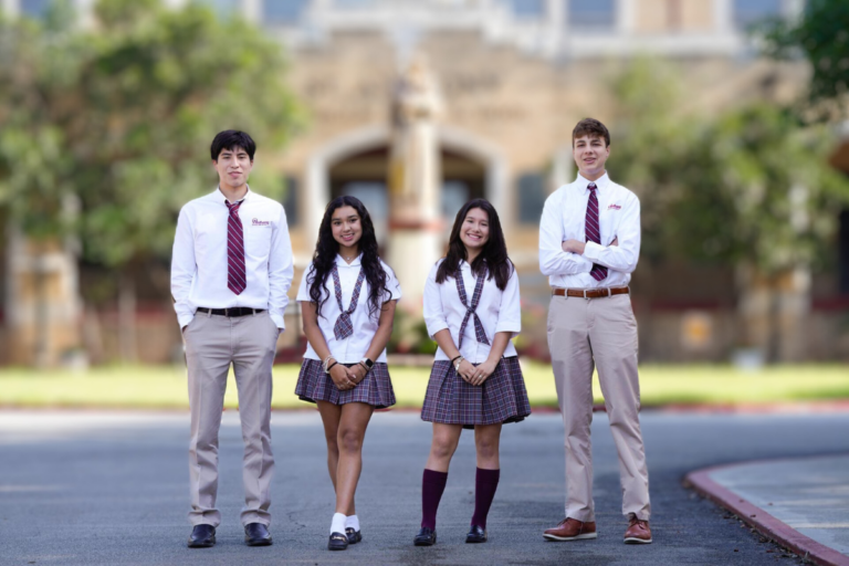Quatro alunos representando a escola de ensino médio (High School) na frente de uma instituição nos EUA com um ambiente escolar ao fundo e um céu claro.